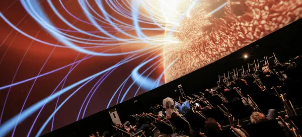 Seated audience watching an immersive dome projection featuring luminous blue light trails and orange abstract visuals.  Copy