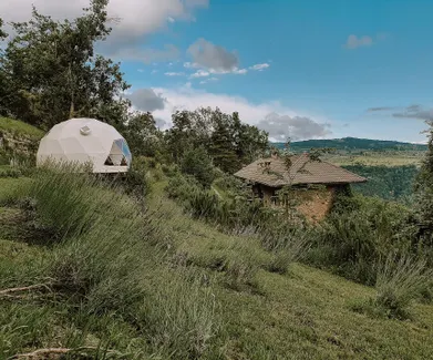 white glamping geodesic dome between green woods and fields