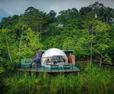 Geodesic glamping dome on a private terrace surrounded by dense tropical forest.