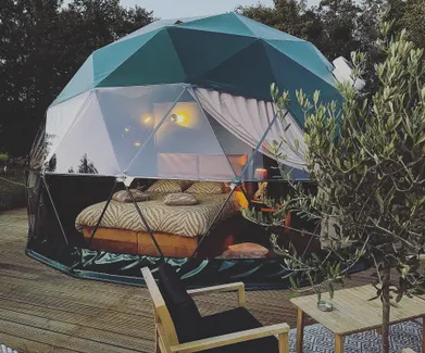 green geodesic dome on wooden deck with a tree and a table with two chairs