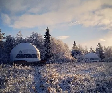 two white glamping geodesic domes in the filed full of snow