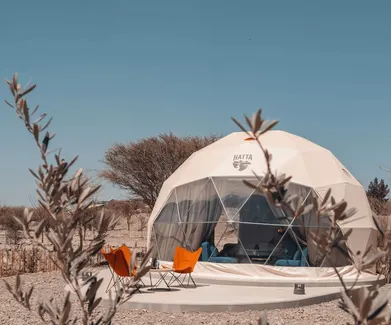 three orange chairs in front of white geodesic dome with logo Hatta on the desert