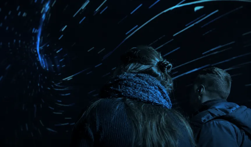 Visitor watching a starfield projection inside a dark immersive dome, with streaks of blue light surrounding the viewing space.