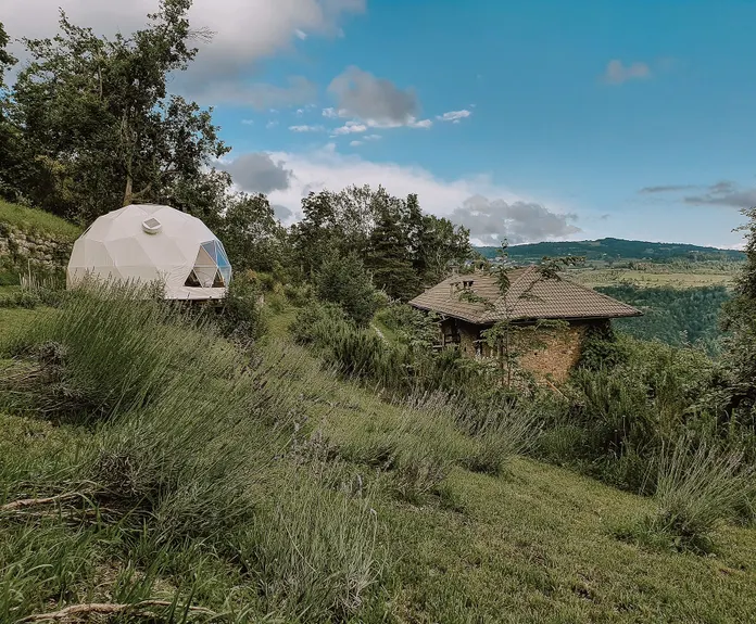 white glamping geodesic dome between green woods and fields