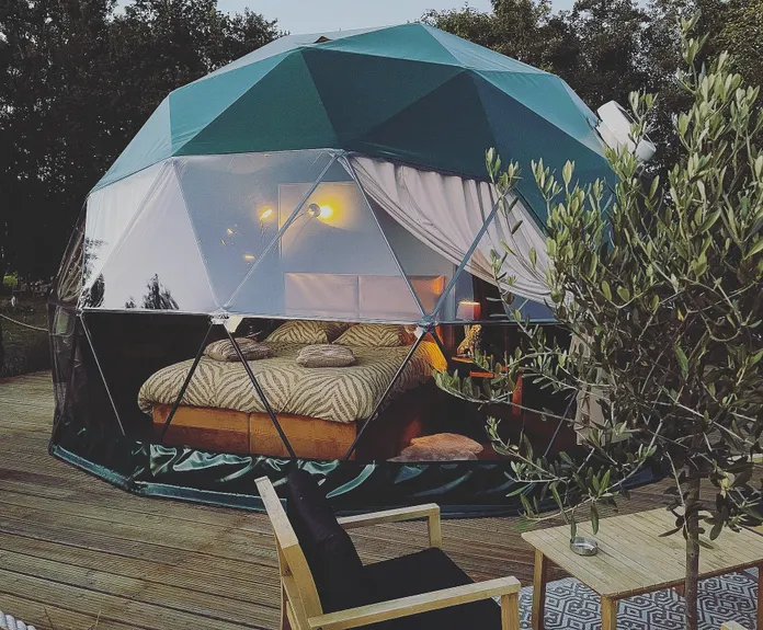 green geodesic dome on wooden deck with a tree and a table with two chairs