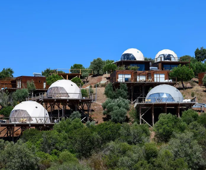 few white glamping geodesic domes on the mountainside with trees