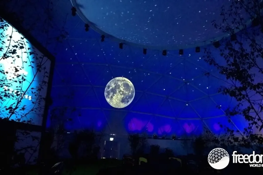Blue-lit geodesic dome interior with a full moon and starfield projected across the curved ceiling.