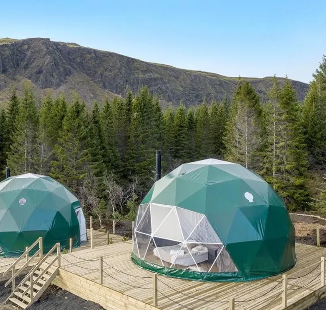 two green geodesic domes on wooden platforms in the forest during the day