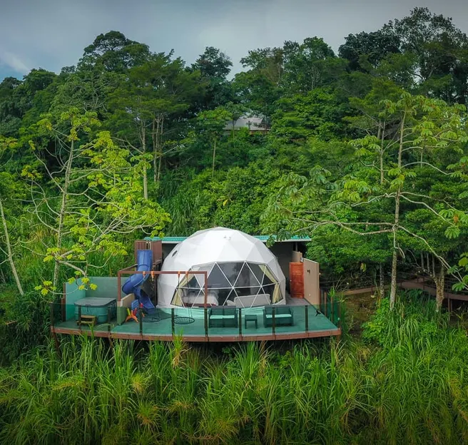 Geodesic glamping dome on a private terrace surrounded by dense tropical forest.