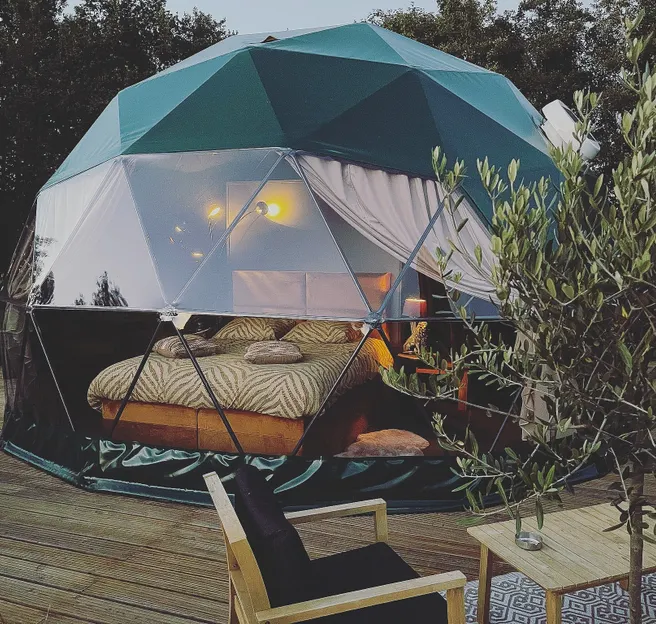green geodesic dome on wooden deck with a tree and a table with two chairs