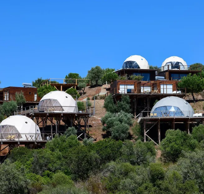 few white glamping geodesic domes on the mountainside with trees