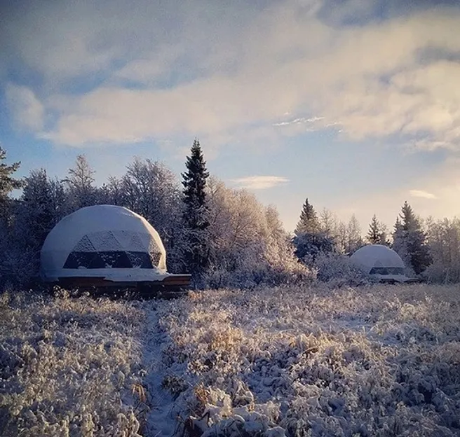 two white glamping geodesic domes in the filed full of snow