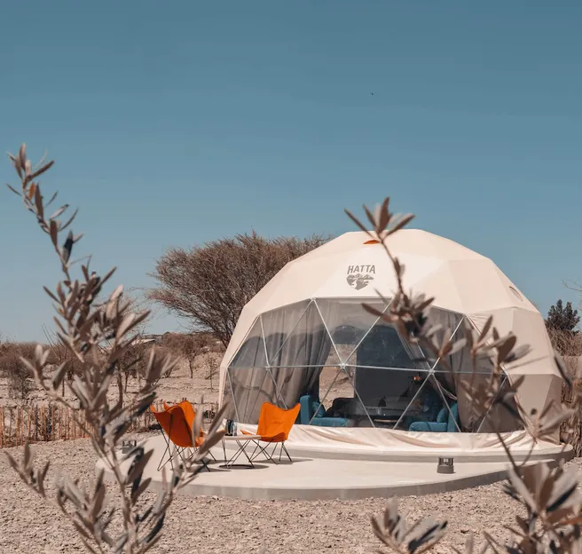 three orange chairs in front of white geodesic dome with logo Hatta on the desert