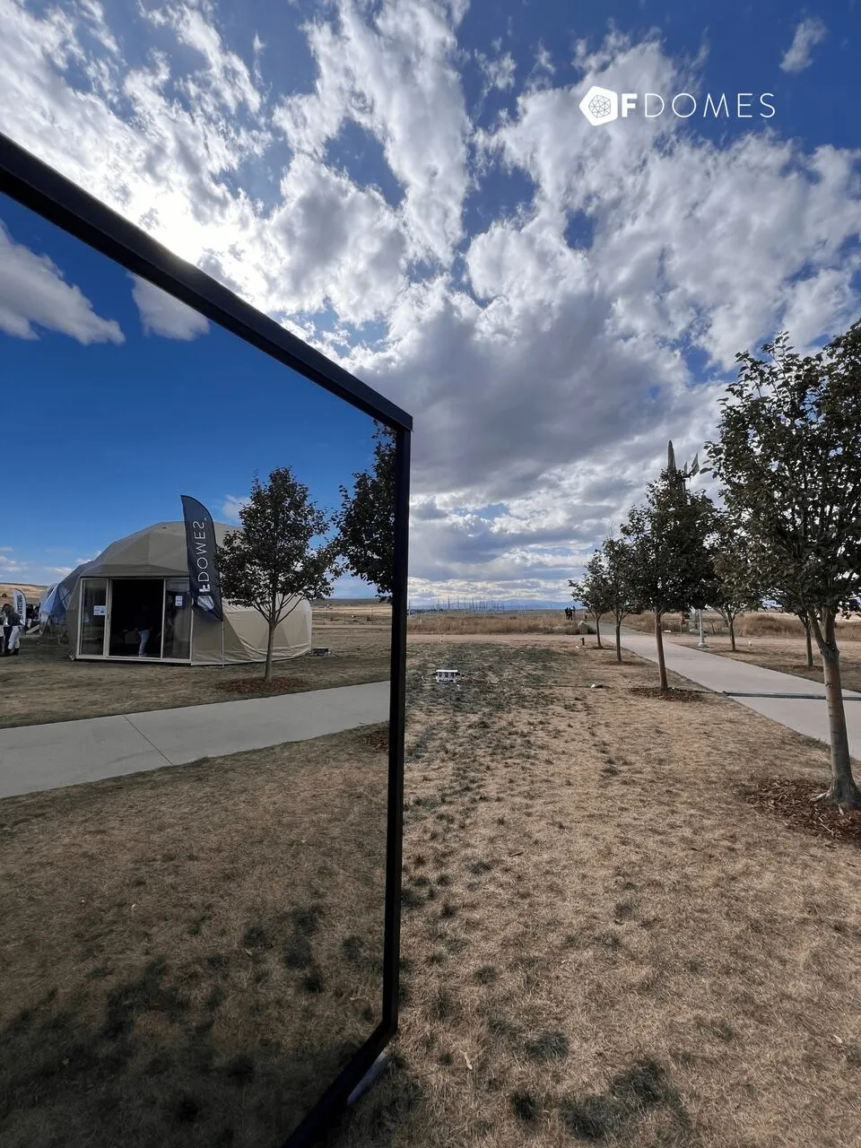 Geodesic dome home with glass facade overlooking a natural landscape and blue cloudy sky.