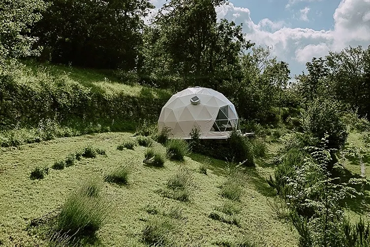 white glamping geodesic dome between green woods