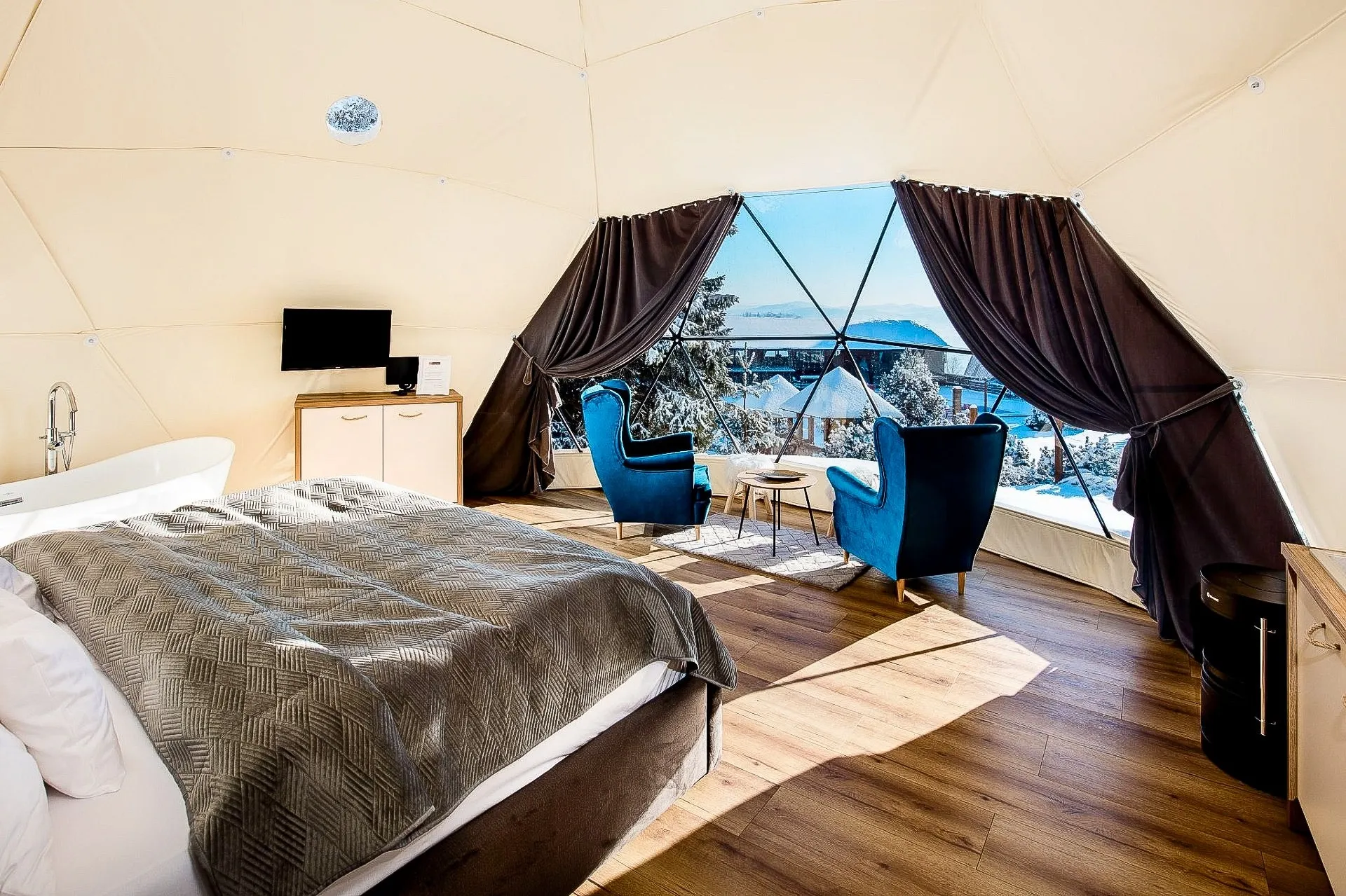 inside of geodesic dome with a bed, two armchairs, a tv and a windows with view