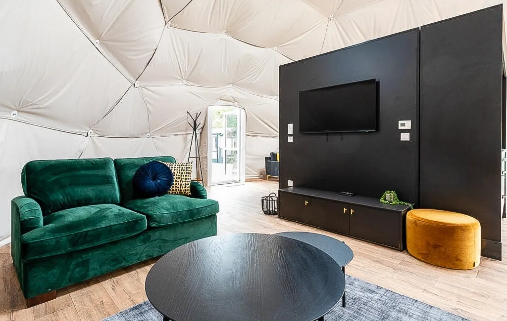 inside of geodesic dome with a sofa, two tables, a carpet and a TV