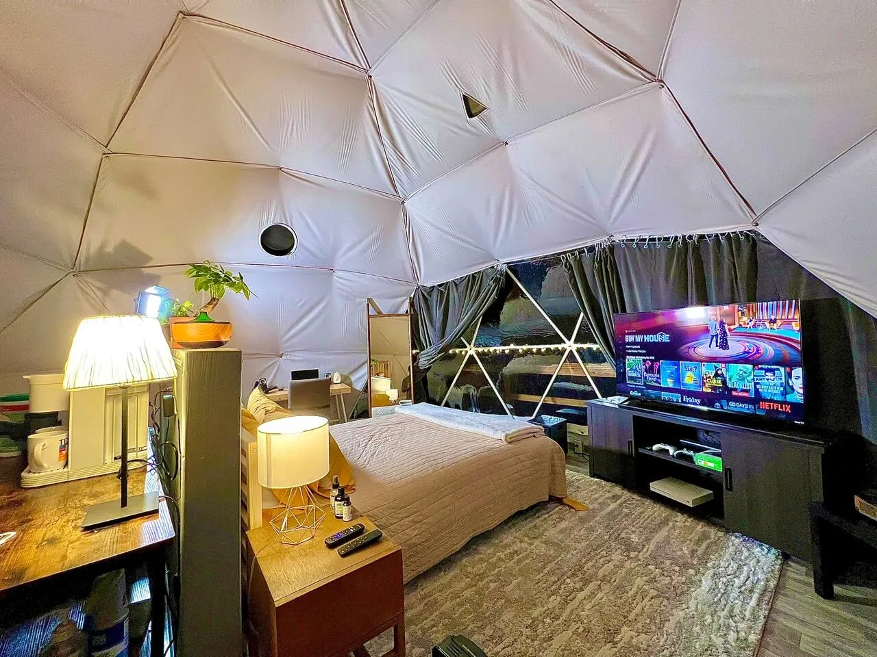 interior of a geodesic dome with a view of the bed, tv and window during the night