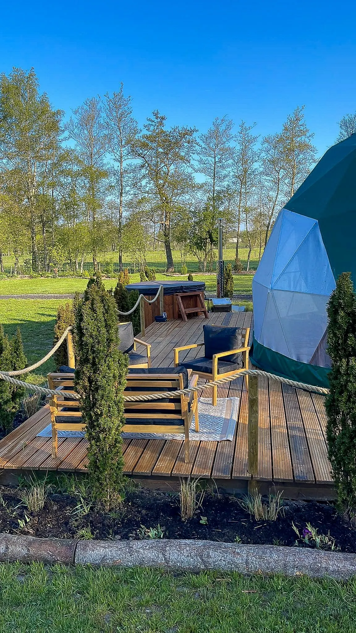 green geodesic dome on wooden deck with a tree and a table with two chairs