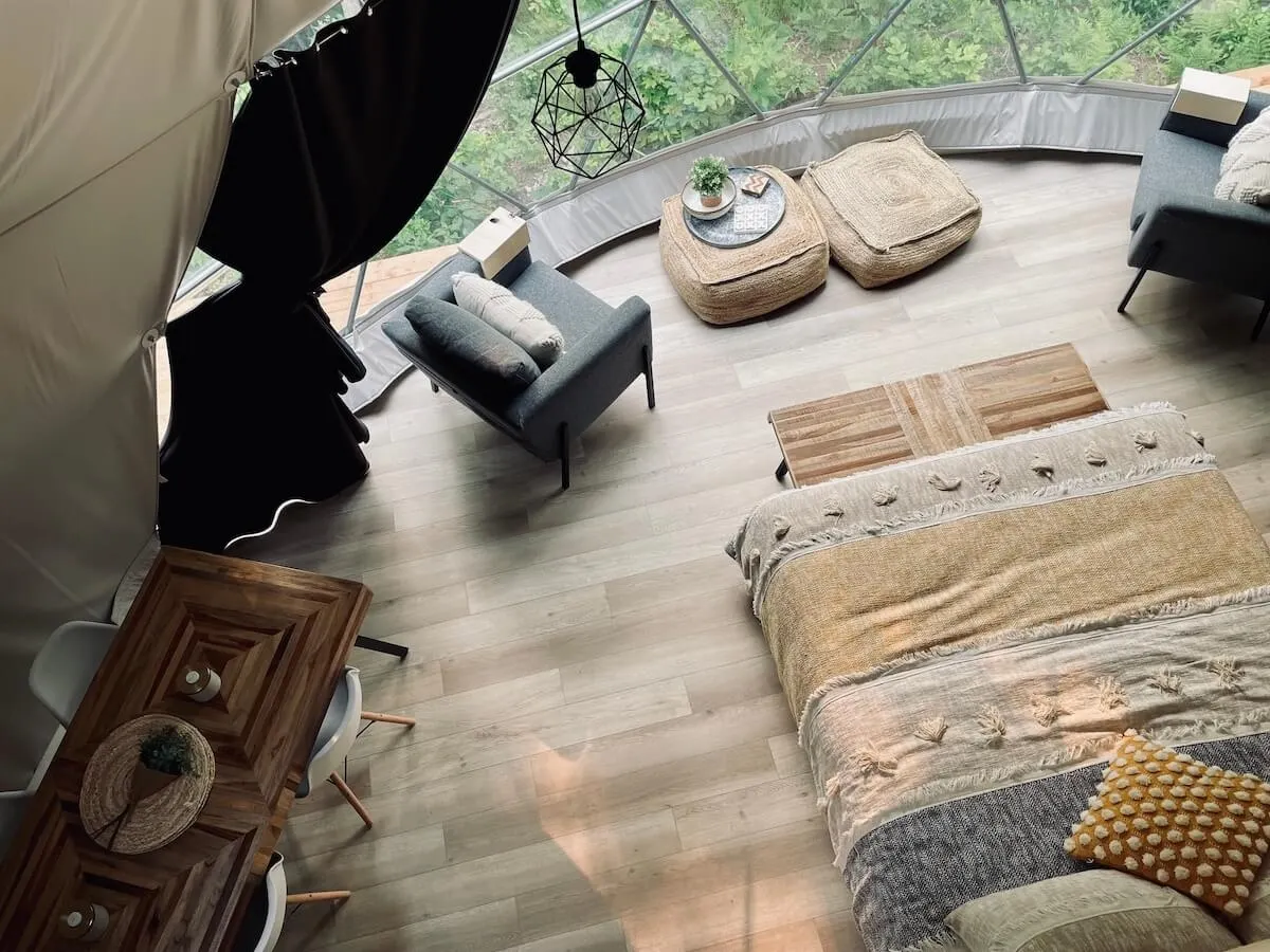 inside of geodesic dome with a bed, two armchairs and a window