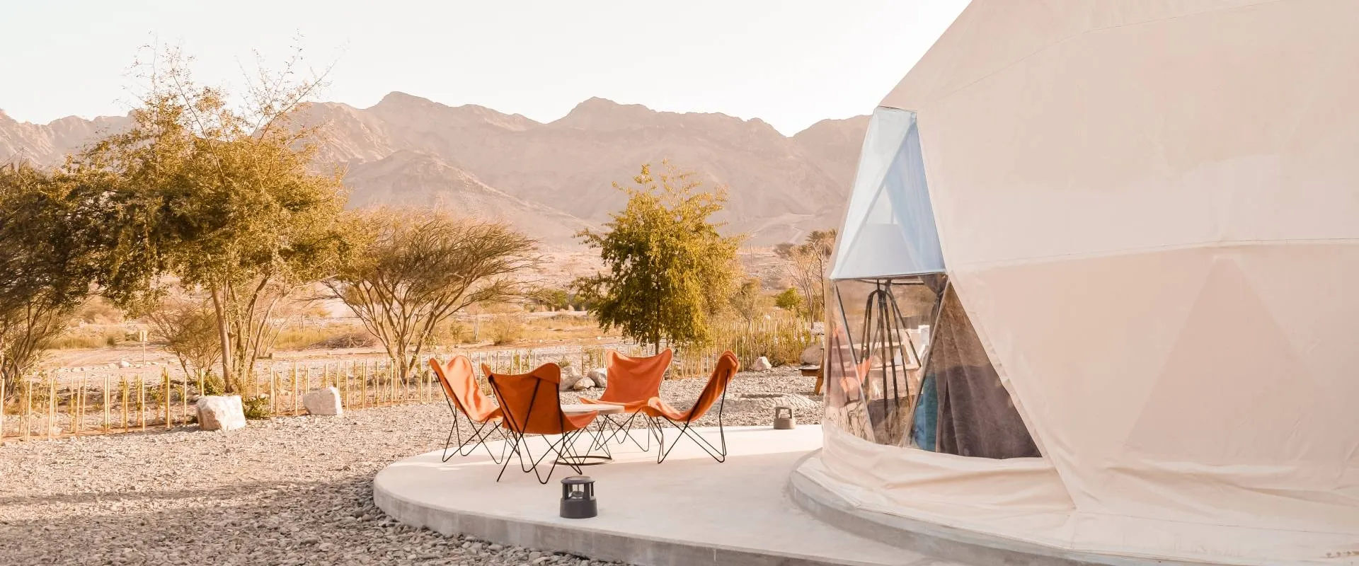 four orange chairs in front of white geodesic dome on the desert