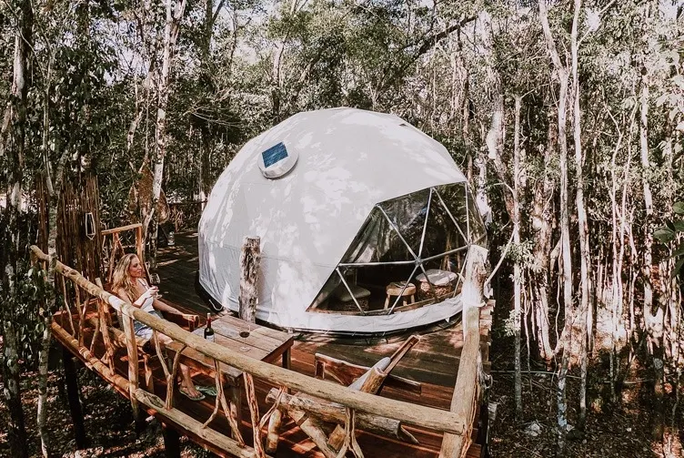 white glamping geodesic dome in behind the trees in the wood
