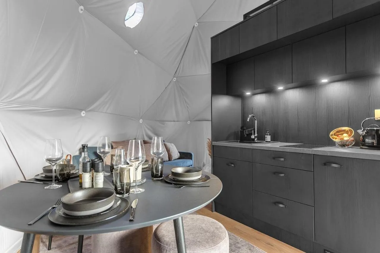 Modern kitchen and dining area inside a geodesic glamping dome, with a set table and black cabinetry.