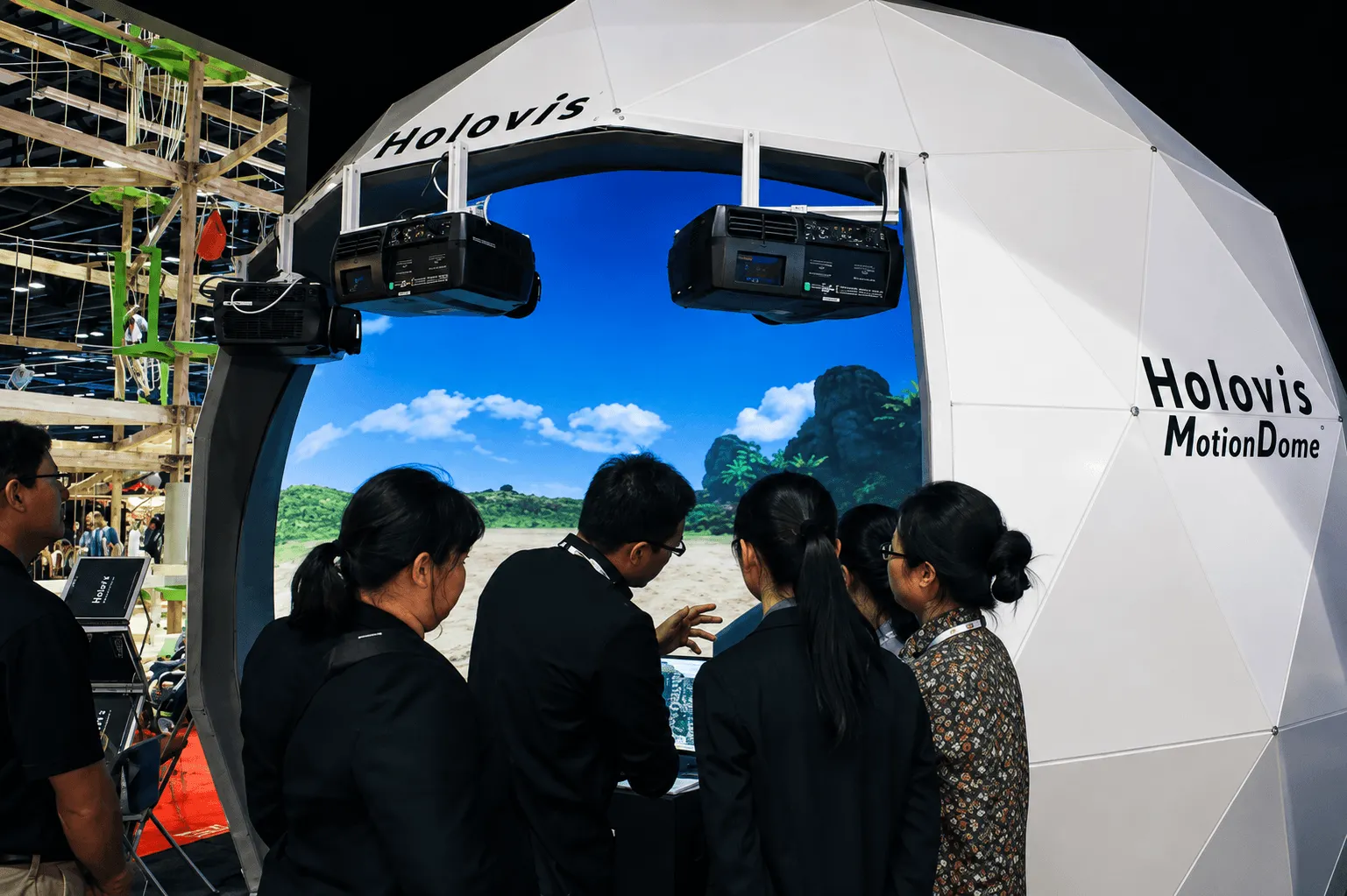 Visitors exploring an interactive motion simulator inside a white geodesic dome at an exhibition, with a large curved display showing a virtual landscape.