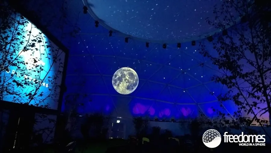 Blue-lit geodesic dome interior with a full moon and starfield projected across the curved ceiling.